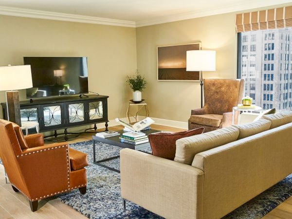 A bright modern living room with sofas, a TV on a stand, a coffee table, lamps, and large windows.